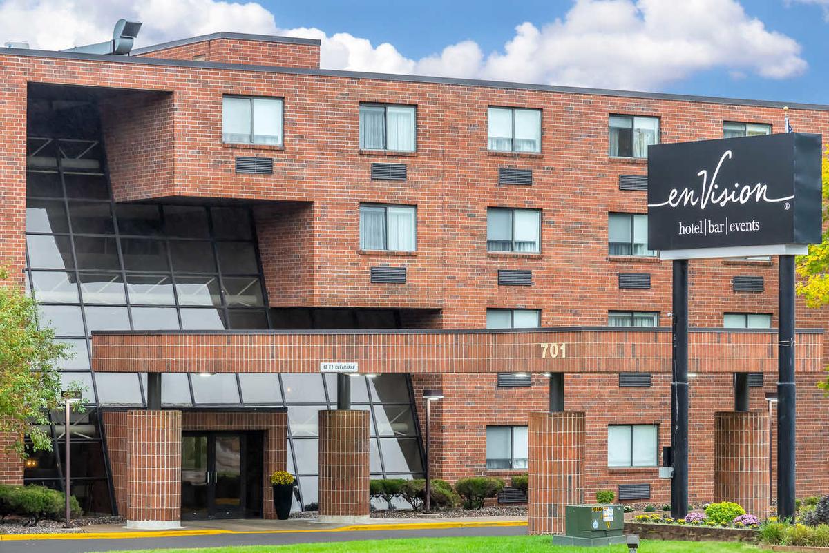 Images shows the exterior of enVision hotel in South Saint Paul. Multi-level brick building with a black sign with white cursive-style lettering.